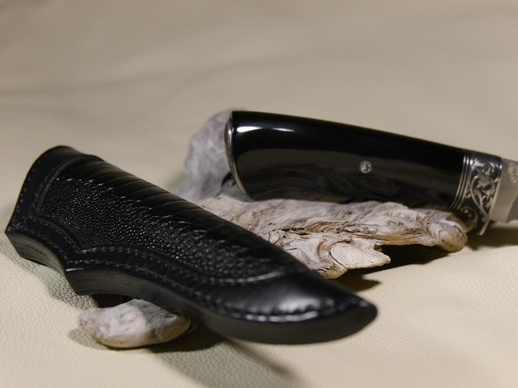 Damastklinge “Feder”, Büffelhorn Griff, graviertes Inlay im Griffende, gravierter Handschutz, Messerscheide: mit Straussenledereinlage.