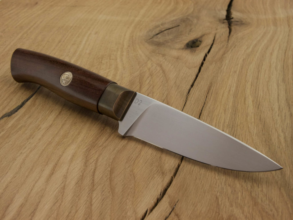 J052-2 Ein handgeschmiedetes Outdoor-Messer mit einem Griff aus Padouk und einer Klinge aus D2-Stahl liegt auf einem Holzbrett.
