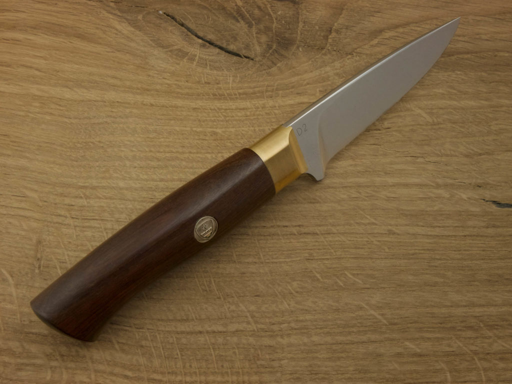 J052-5 A hand forged outdoor knife with an African Coral Wood handle and blade from D2 steel lays on a wooden board.