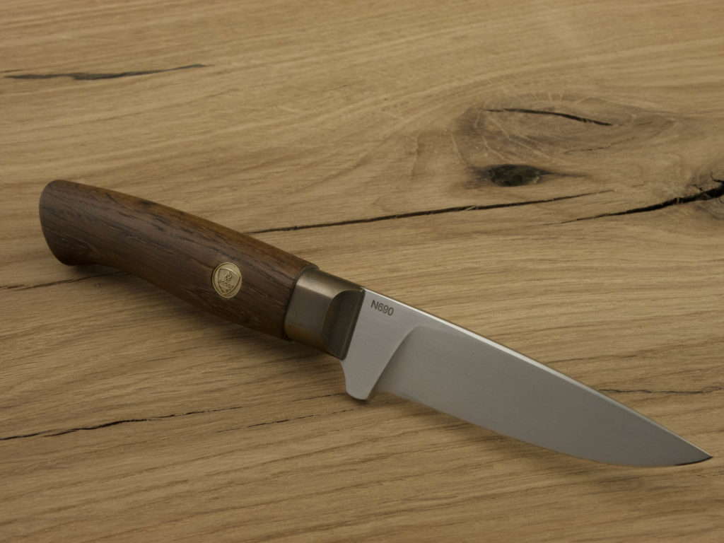 J054-3 Ein handgeschmiedetes Outdoor-Messer mit einem Griff aus geräucherter Eiche und einer Klinge aus N690-Stahl liegt auf einem Holzbrett.