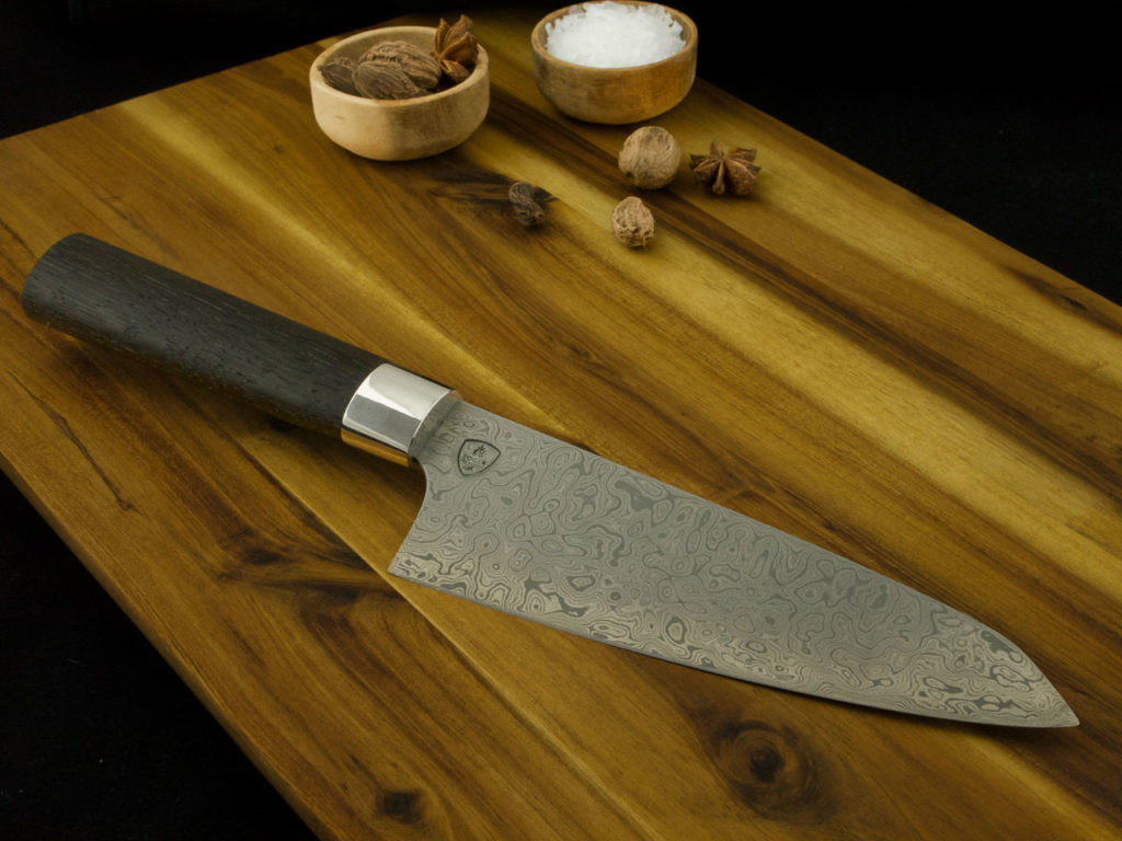 K021-4 Custom Santoku kitchen knife with a Damascus steal blade and handle from Bog Oak lays on a wooden cutting board.